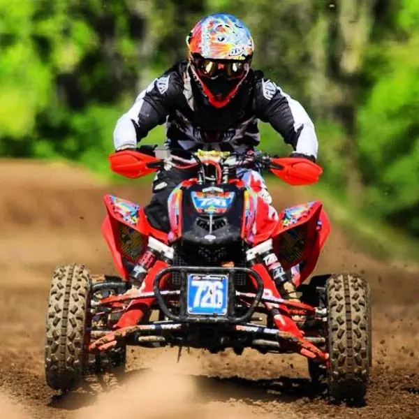 A person on a red and black atv riding through mud.